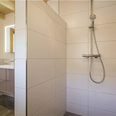 Eine moderne Dusche mit fliesenverkleideten Wänden. Der Raum ist hell und elegant eingerichtet.