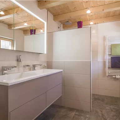 Ein modernes Badezimmer mit hellen Fliesen und einem großen Spiegel. Die Holzdecke und die Handtücher verleihen dem Raum eine gemütliche Atmosphäre.