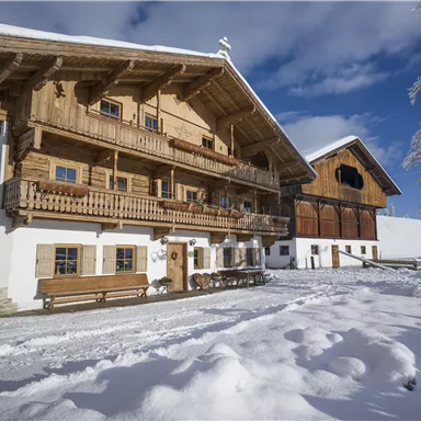 Ein traditionelles Holzhaus in einer verschneiten Landschaft. Der Himmel ist klar und blau, und die Umgebung ist ruhig und winterlich.