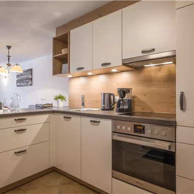 Eine moderne Küche mit hellen Schränken und einer Arbeitsplatte aus Holz. Die Ausstattung umfasst einen Herd, eine Kaffeemaschine und genügend Stauraum.