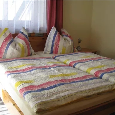 Ein gemütliches Schlafzimmer mit einem großen Doppelbett und bunten Bettdecken. Weiche Kissen und ein warmes Licht sorgen für eine einladende Atmosphäre.