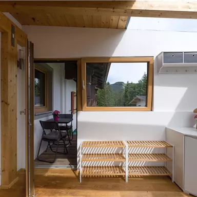 Ein helles Zimmer mit Holzdetails und großen Fenstern. Es gibt einen kleinen Tisch mit Stühlen und dekorative Pflanzen.