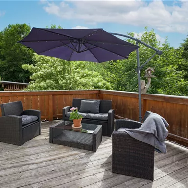 Eine gemütliche Terrassen-Ecke mit einem Sonnenschirm und stilvollen Möbeln. Umgeben von grünem Laub und einem Holzgeländer.