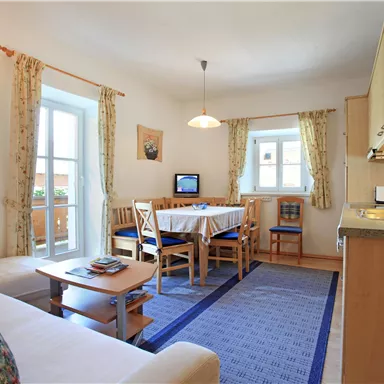 Ein helles Wohnzimmer mit einem Esstisch und Stühlen. Die Küche ist gut ausgestattet, und es gibt große Fenster, die viel Licht hereinlassen.