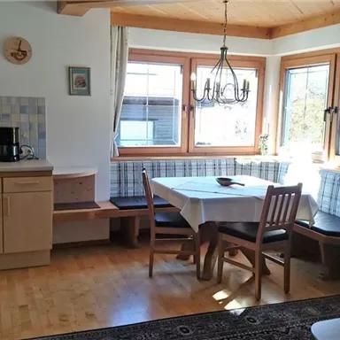 Eine helle Küche mit Holzregalen und einem Esstisch. Große Fenster sorgen für viel Tageslicht.