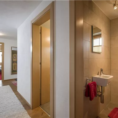 Ein heller Flur mit modernen Türen und einem kleinen Badezimmer auf der rechten Seite. Der Boden ist mit einem Teppich bedeckt und das Licht ist gemütlich.