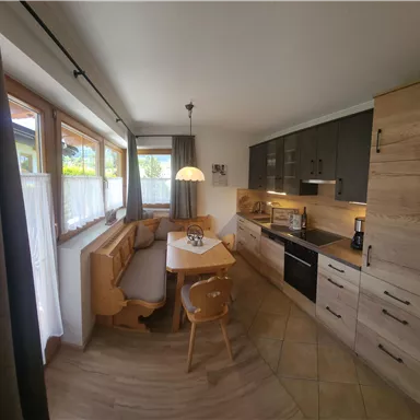 Eine moderne Küche mit Holzschränken und einem gemütlichen Essbereich. Große Fenster sorgen für viel Tageslicht.