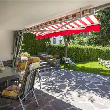 An inviting terrace with a dining area and a sun umbrella. The garden is green with plenty of outdoor seating.