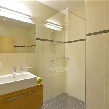A modern bathroom with bright walls and a glass shower. It features a sink with a wooden cabinet and fresh towels.