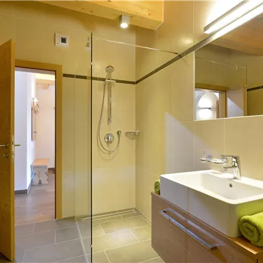 A modern bathroom with a glass shower and a simple sink. The walls are light, and wooden details create a cozy atmosphere.
