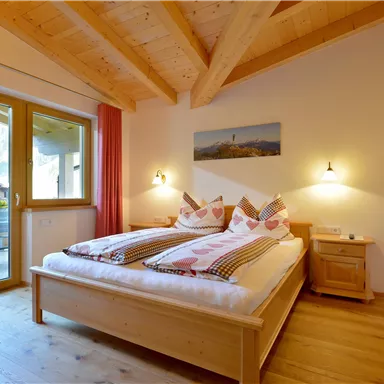 An inviting bedroom with a wooden ceiling and two single beds. The room has large windows with a view and cozy decoration.