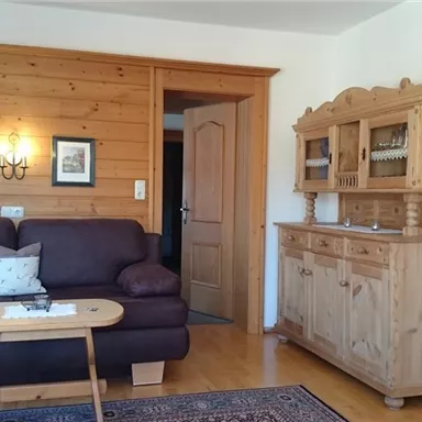 Ein gemütliches Wohnzimmer mit einem braunen Sofa und einem Holztisch. An der Wand befinden sich Holzverkleidungen und Bilderrahmen, sowie ein Sideboard aus Holz.
