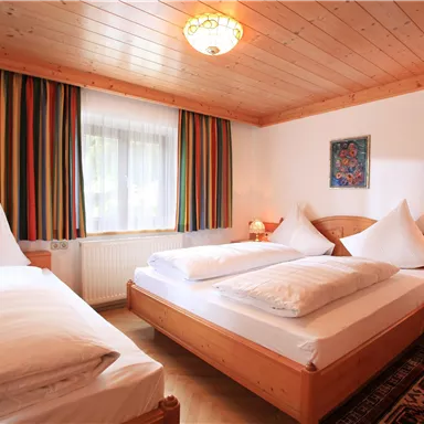 Ein gemütliches Schlafzimmer mit zwei Betten und einem zusätzlichen Einzelbett. Das Zimmer hat Holzdetails und farbige Vorhänge, die einladend wirken.