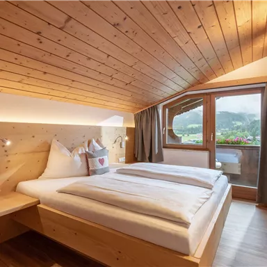 Ein gemütliches Schlafzimmer mit Holzdecke und zwei Betten. Große Fenster bieten einen Blick auf die Landschaft.