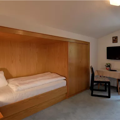 A simple room with a bed, a table, and two chairs. There is a television and a window with a view.