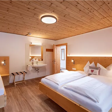 Ein gemütliches Schlafzimmer mit zwei Betten und warmem Holzdekor. Es gibt einen kleinen Tisch und einen Waschbereich im Raum.