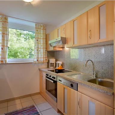 Eine moderne Küche mit Holzschränken und einem Fenster mit Blick ins Grüne. Sie ist ausgestattet mit einem Herd, einer Spüle und einer Kaffeemaschine.