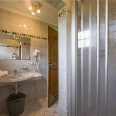 Ein modernes Badezimmer mit einer Dusche und einem Waschbecken. Die Wände sind hell gefliest, und es gibt Handtücher sowie einen Spiegel.