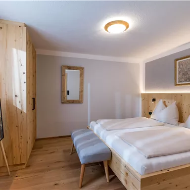 Ein modernes Schlafzimmer mit Holzdekor und zwei Betten. Der Raum ist hell und gemütlich und verfügt über einen Fernseher und einen Spiegel.