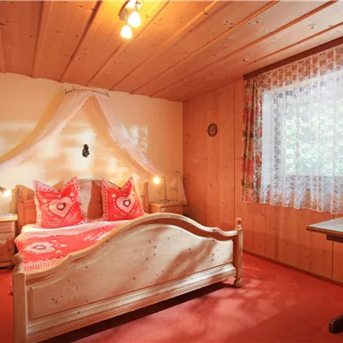 A cozy bedroom with a wooden bed and red-and-white bedding. The room has a warm atmosphere with wood paneling and a small table.