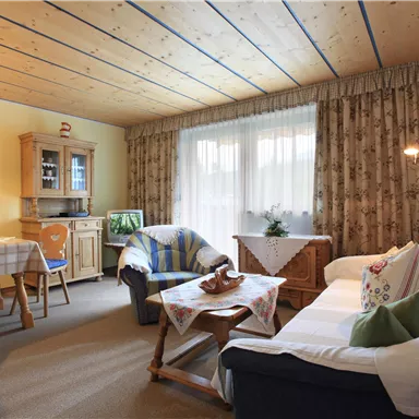 A cozy living room with a white sofa and a wooden table.  
Large windows let in plenty of light, and the walls are decorated in bright colors.