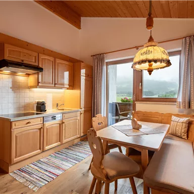 Eine gemütliche Küche aus Holz mit einem Esstisch und Bänken. Ein Fenster bietet Blick auf die umliegende Landschaft.