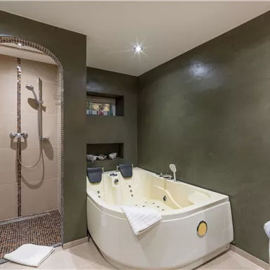 Ein modernes Badezimmer mit einer hellen Badewanne und einer Regendusche. Die Wände sind in einem eleganten Grauton gestrichen und es liegt ein Handtuch auf dem Boden.