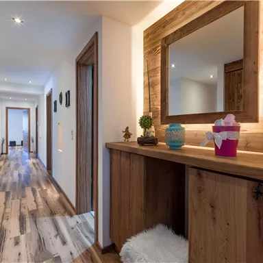Ein heller Flur mit Holzfußboden und stilvollen Wänden. Auf der Kommode stehen dekorative Elemente und ein Spiegel.