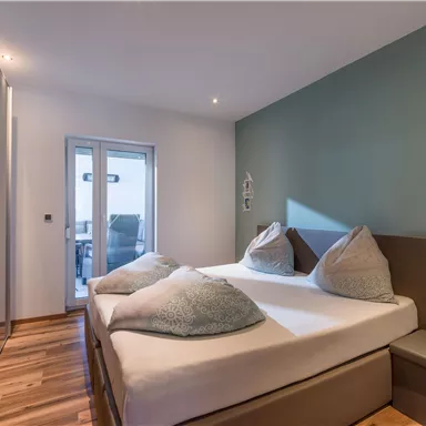 Ein modernes Schlafzimmer mit einem großen Doppelbett und komfortablen Kissen. Die Wände sind in sanften Farben gestrichen, und es gibt Zugang zu einem Balkon.