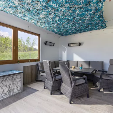 Ein gemütlicher Aufenthaltsraum mit modernen Möbeln und großen Fenstern. Die Decke ist mit einem farbigen Netz dekoriert, das eine entspannte Atmosphäre schafft.