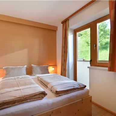 Ein gemütliches Schlafzimmer mit zwei Einzelbetten und warmen Farben. Das Fenster bietet einen Blick auf die grüne Landschaft.