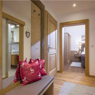 An inviting hallway with wood-paneled walls and a large mirror. Red cushions and warm light create a cozy atmosphere.