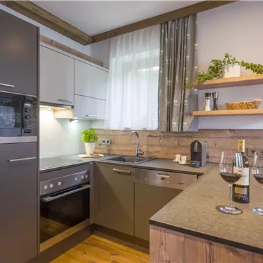 A modern kitchen with bright cabinets and wooden details. On the countertop are two wine glasses and a bottle of wine.