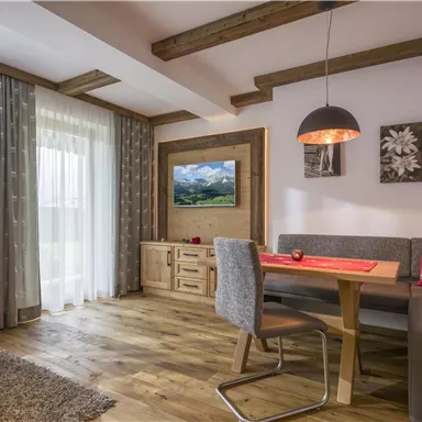 A modern living room with a wooden ceiling and a dining area. The windows provide plenty of natural light, and the decor is cozy and inviting.