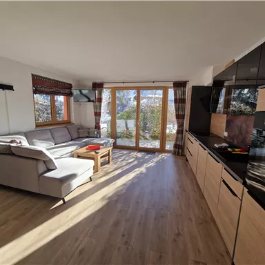 A modern living room with a gray sofa and a wooden table. Large windows provide plenty of daylight and a view outdoors.
