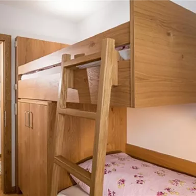Ein gemütliches Schlafzimmer mit einem Hochbett aus Holz. Die Wände sind hell, und der Raum wirkt freundlich und einladend.