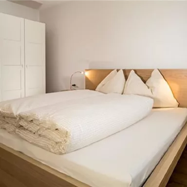 Ein gemütliches Schlafzimmer mit einem Doppelbett und hellen Holzdetails. Neben dem Bett befindet sich ein moderner Nachttisch und ein Kleiderschrank.