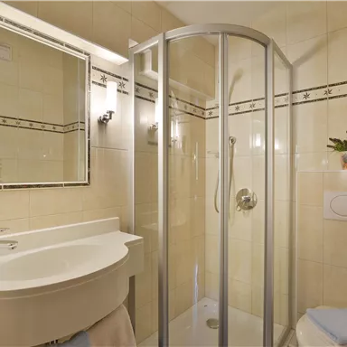 A modern bathroom with a shower and a sink. The walls are brightly tiled and designed with decorative elements.