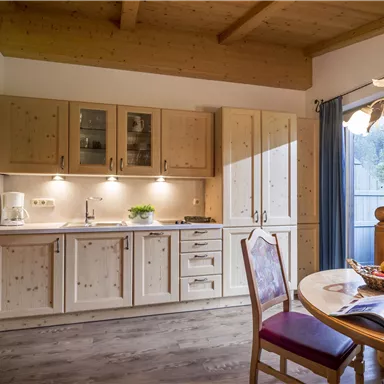 A modern kitchen with wood cabinets and a bright countertop. There is fruit on the table and windows looking outside.