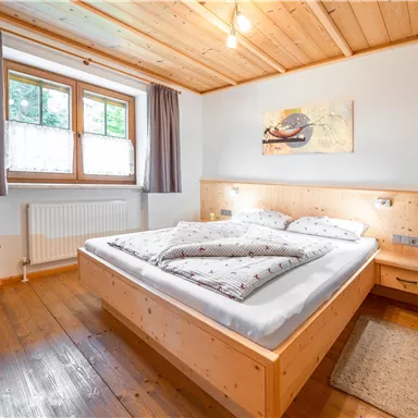 Ein gemütliches Schlafzimmer mit einem Doppelbett und Holzverkleidung. Große Fenster sorgen für viel Tageslicht und eine einladende Atmosphäre.