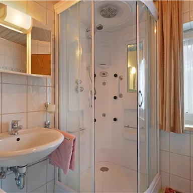 A bathroom with a modern shower and a sink. Bright tiles and a window create a friendly atmosphere.