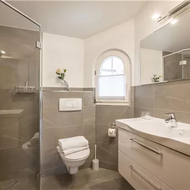 Ein modernes Badezimmer mit einer Dusche und einem großen Spiegel. Die Wände sind in neutralen Grautönen gehalten.