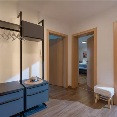 Ein heller Flur mit einem modernen Kleiderständer und einem kleinen Tisch. Im Hintergrund sind zwei offene Türen zu weiteren Räumen sichtbar.