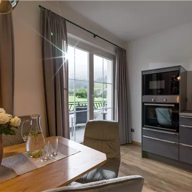 Eine moderne Küche mit einem Essbereich und großen Fenstern. Es gibt einen Blick ins Freie und eine ansprechende Dekoration mit Blumen.