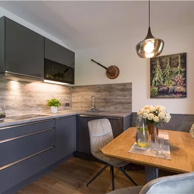 Eine moderne Küche mit dunklen Schränken und einem gemütlichen Essbereich. Der Tisch ist mit Blumen und einem rustikalen Bild dekoriert.