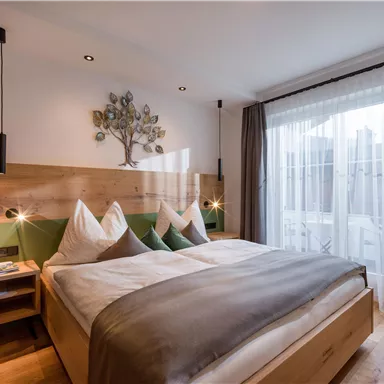 Ein modernes Schlafzimmer mit einem komfortablen Doppelbett und Holzmöbeln. Große Fenster garantieren viel Licht und einen schönen Blick nach draußen.