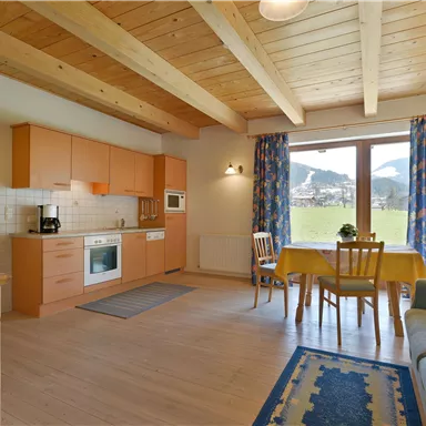 Eine helle, moderne Küche mit Holzdecke und großen Fenstern. Ein Essbereich mit Tisch und Stühlen bietet einen Blick auf die Natur.