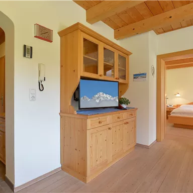 Eine helle und gemütliche Küche mit Holzschränken und einem Fernseher. Im Hintergrund ist ein Zugang zu einem Schlafzimmer zu sehen.