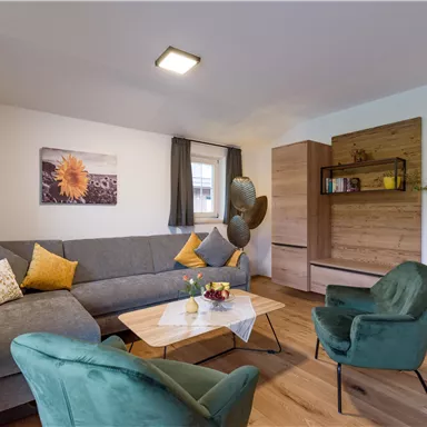 Ein modernes Wohnzimmer mit einem grauen Sofa und grünen Stühlen. Ein Tisch mit Blumen und ein Holzregal sorgen für eine gemütliche Atmosphäre.