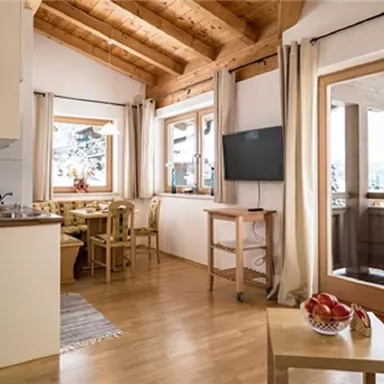 Ein modernes Wohnzimmer mit Holzdecke und großen Fenstern. Es gibt eine gemütliche Sitzecke und einen Esstisch mit Blick auf die Berge.